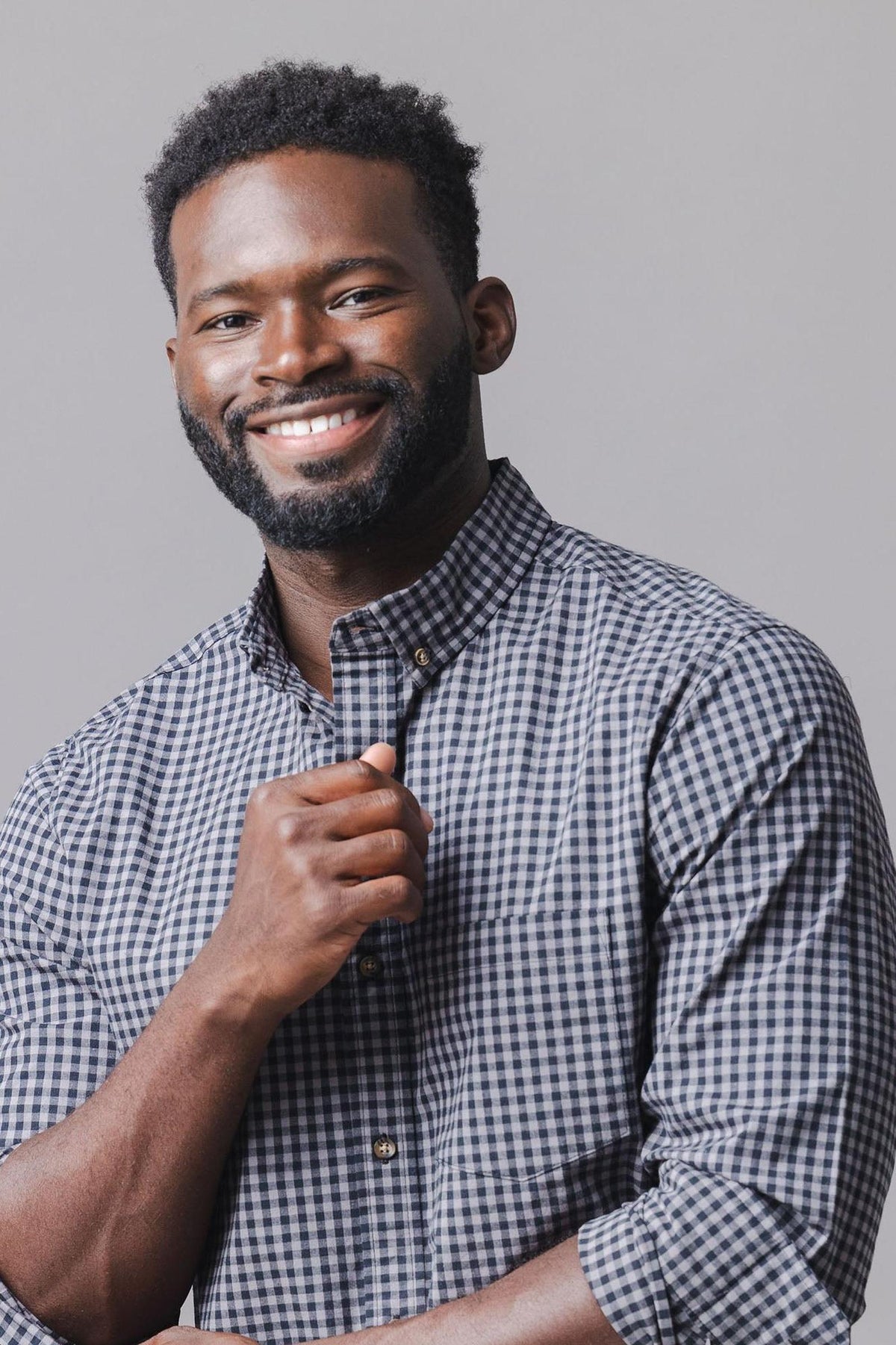 A smiling man wears a black gingham long sleeve button-down shirt made from soft stretch organic cotton. The shirt features a button closure and a functional chest pocket.