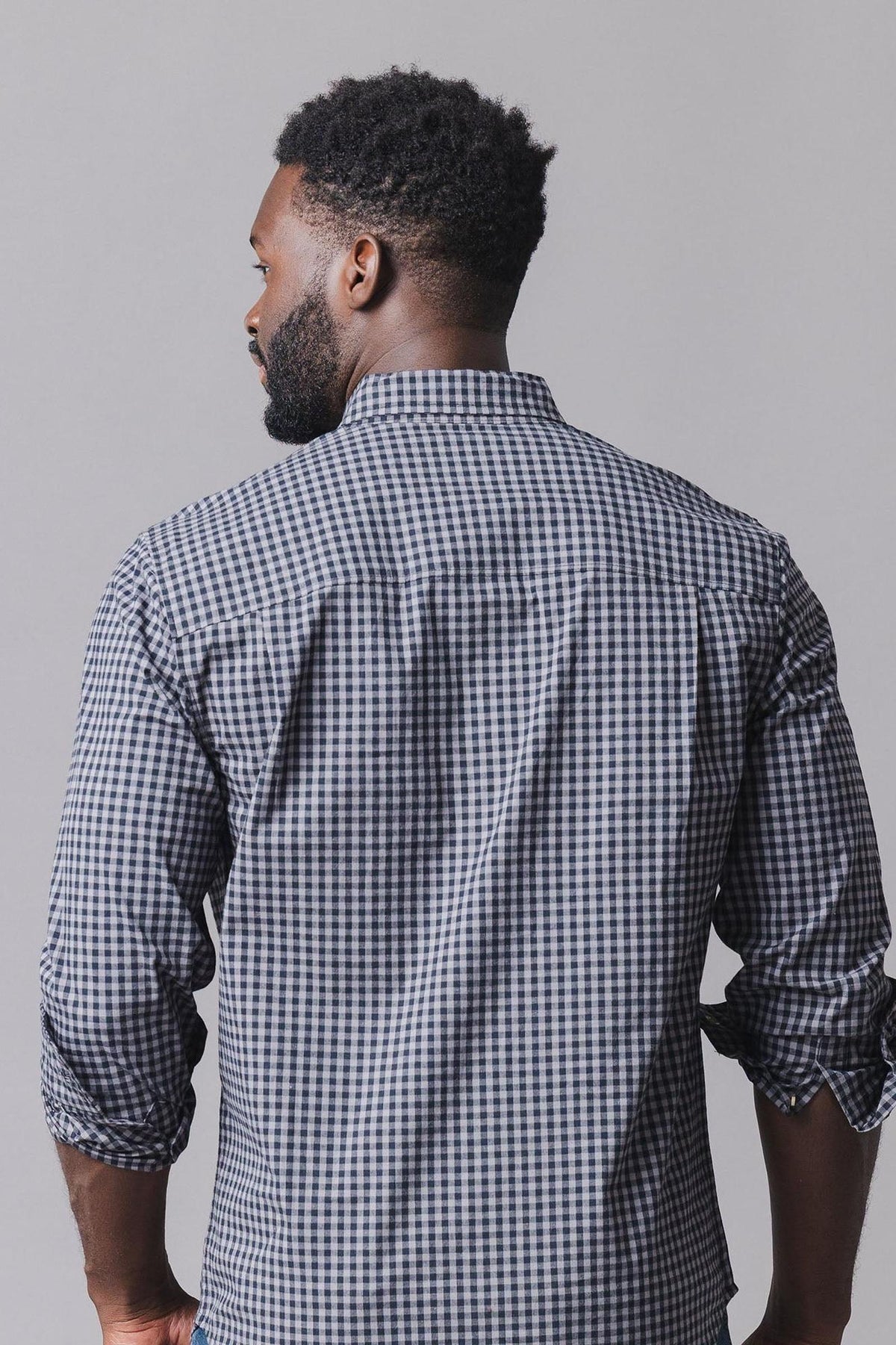 A man is seen from behind, wearing a black gingham organic cotton poplin shirt with long sleeves.