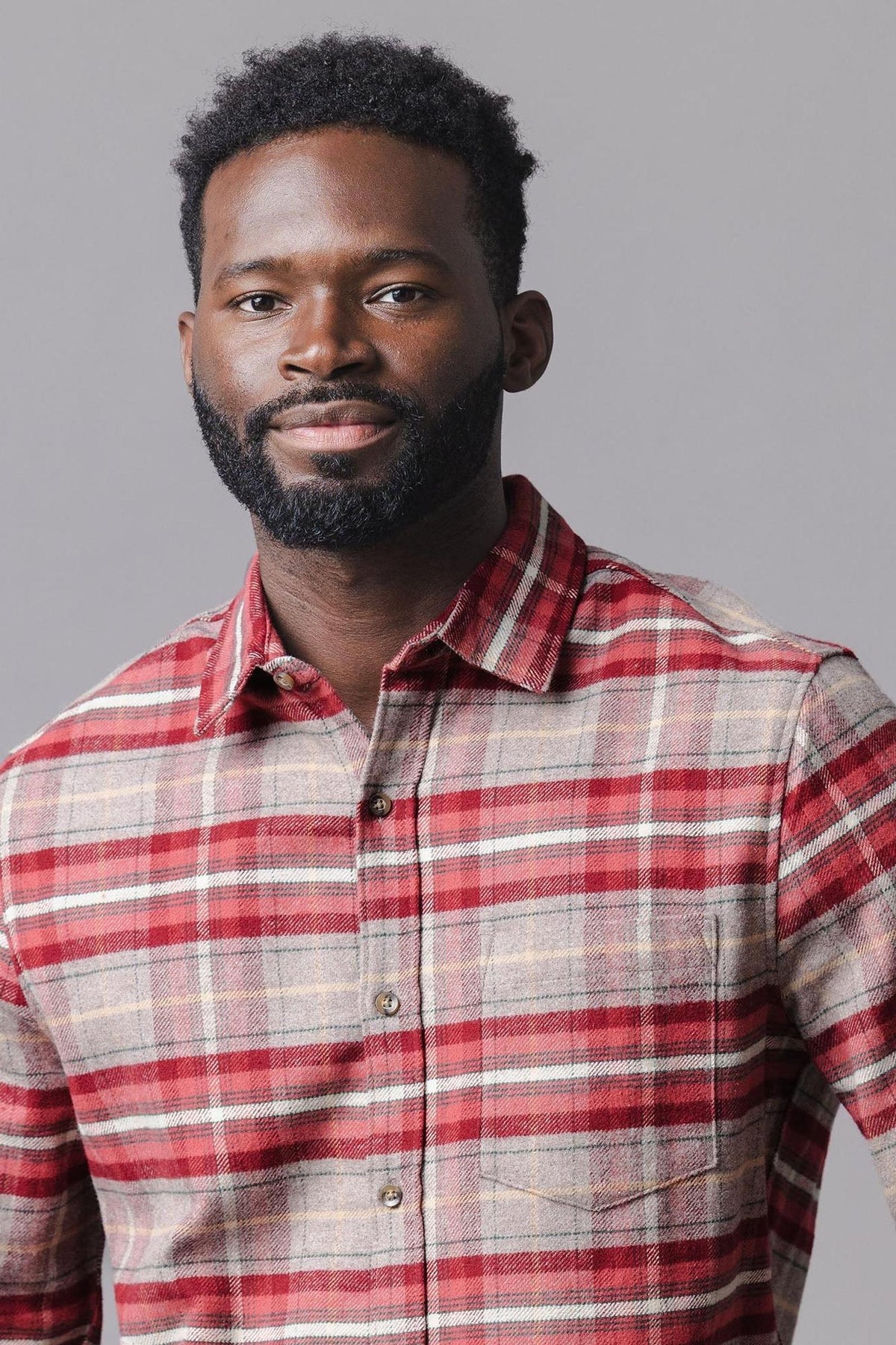 A man models a button-down shirt featuring a rosy taupe plaid pattern. The shirt is made from soft, sustainable flannel, highlighting its organic cotton material and cozy design.