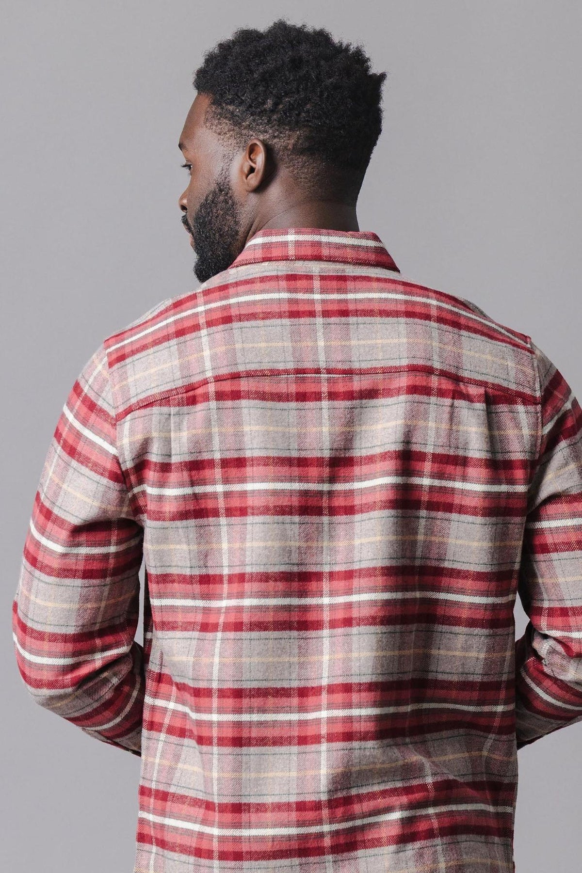 A man is wearing a cozy, organic cotton flannel shirt in rosy taupe plaid. The shirt features a button-down style and is seen from the back against a neutral background.