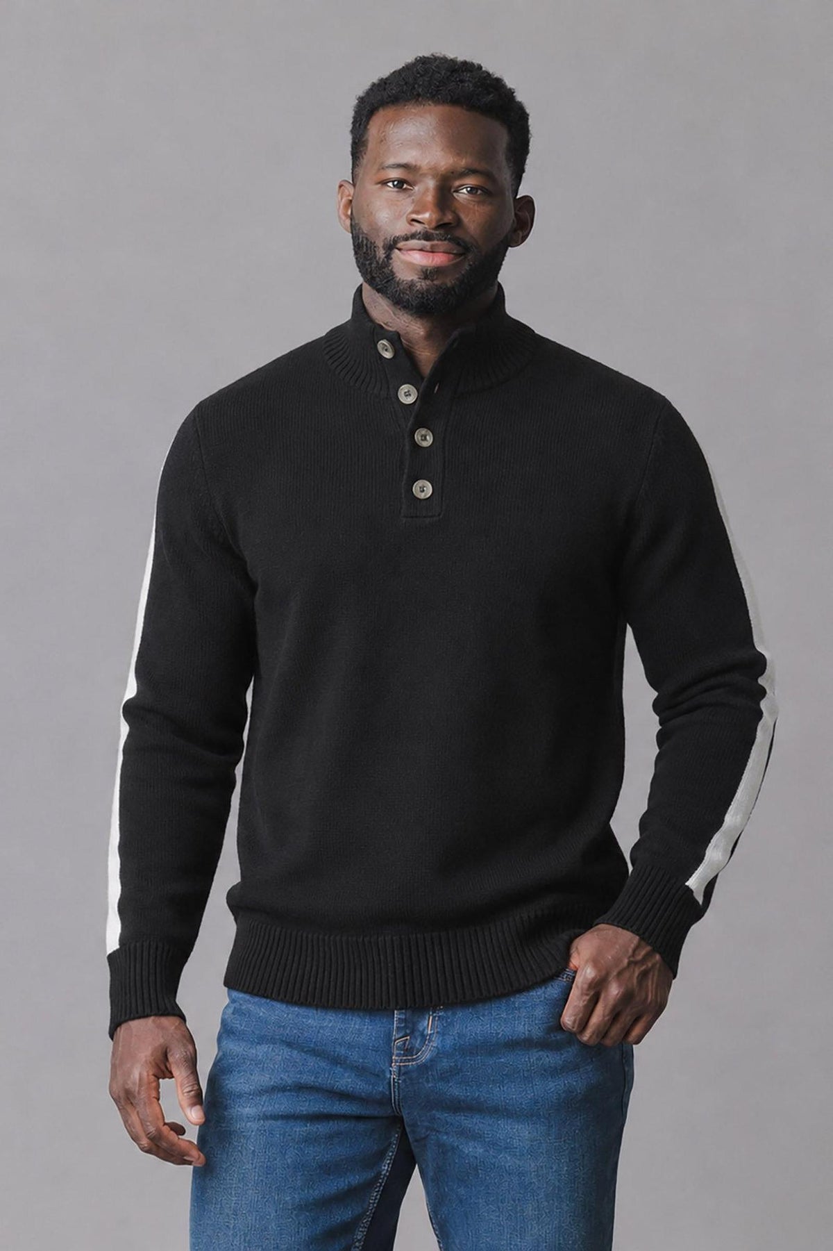 A man wearing a black organic mock neck sweater with a short Henley button placket and white stripes on the outer sleeves stands against a neutral background.