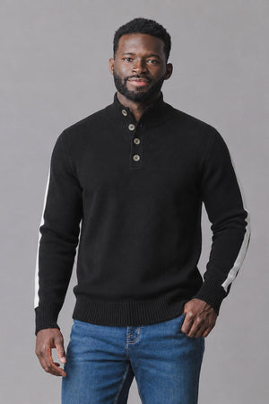 A man wearing a black organic mock neck sweater with a short Henley button placket and white stripes on the outer sleeves stands against a neutral background.