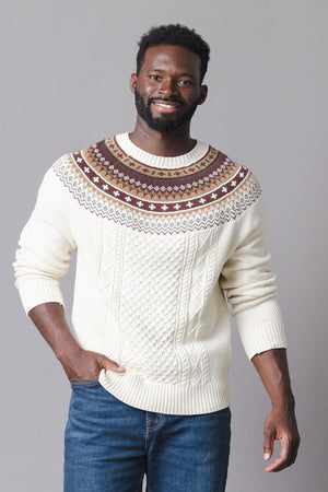 A man models a cozy ivory sweater featuring a fair isle design in brown and red at the shoulders, complemented by a textured cable knit pattern.