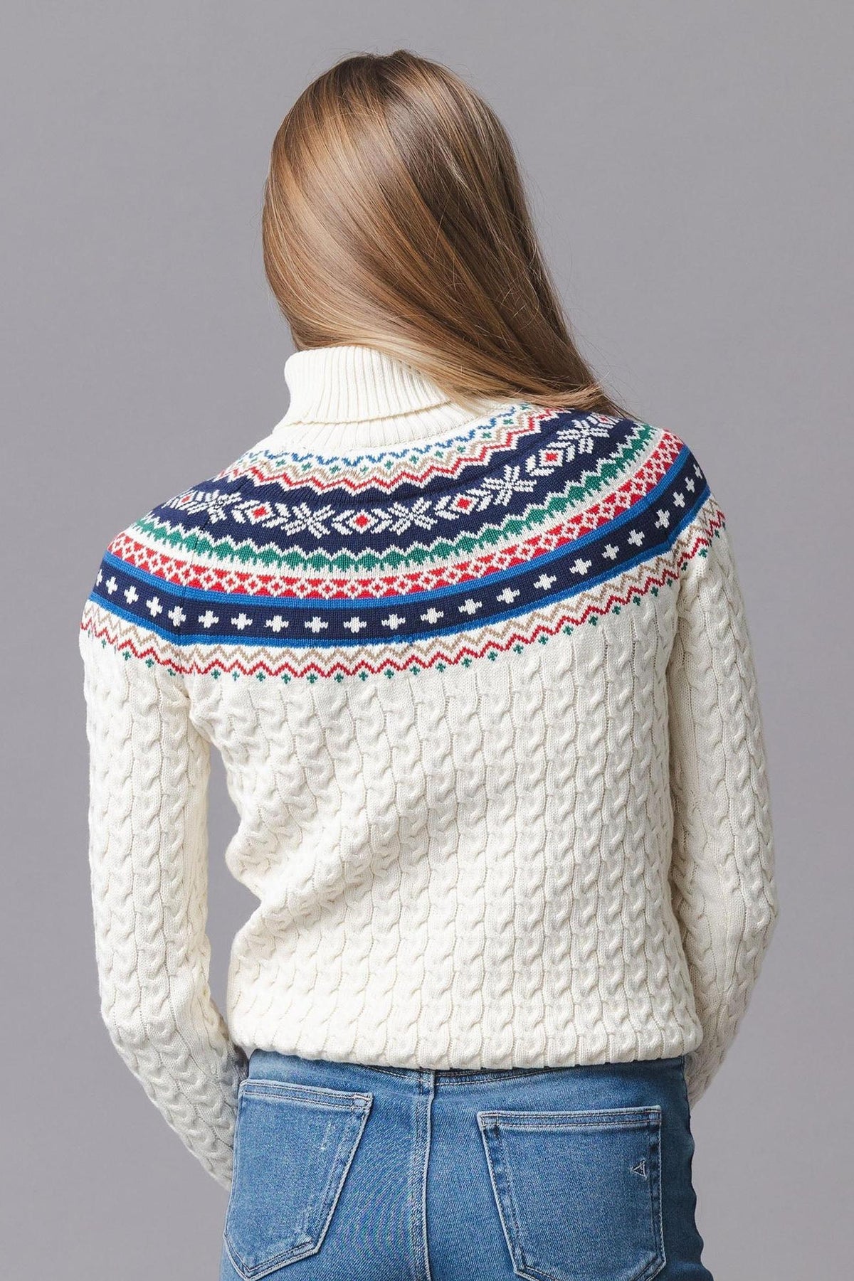 A woman is seen from the back, wearing an ivory organic cotton sweater with a fair isle design in red, blue, and green across the shoulders.