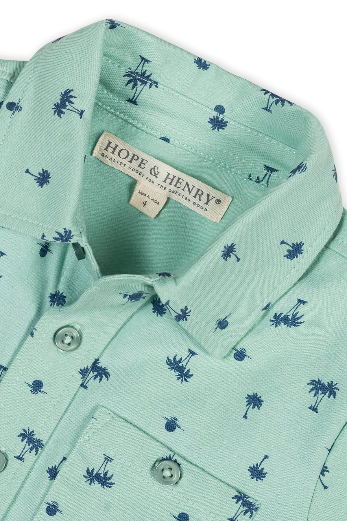 Close-up of a mint green button-down shirt featuring a playful palm tree print. Made from soft organic cotton, it is designed for kids, offering comfort and a stylish summer look.