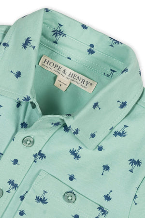 Close-up of a mint green button-down shirt featuring a playful palm tree print. Made from soft organic cotton, it is designed for kids, offering comfort and a stylish summer look.