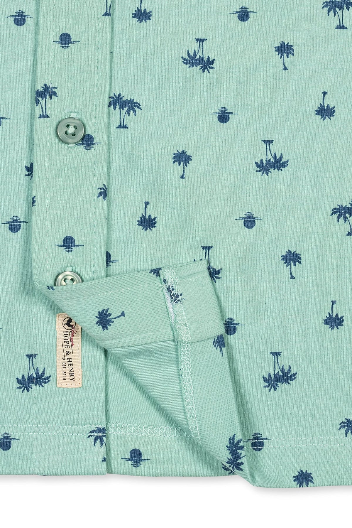 Light green organic cotton jersey button-down shirt featuring a playful navy palm tree and sun print. Designed for kids, this shirt combines comfort with a classic tropical style.