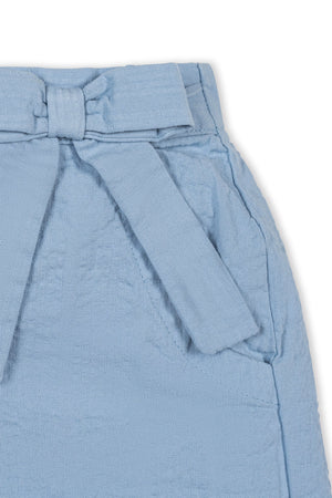 Close-up of a light blue organic cotton seersucker pull-on short featuring a decorative bow and faux belt detail. Ideal for warm weather play, suitable for children ages 2T to 12.