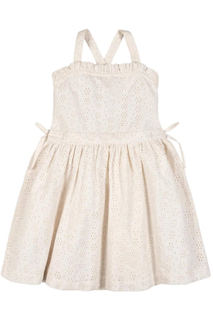 A light beige organic cotton eyelet dress features feminine ruffle edges and crossback straps. The dress is fully lined and designed for summer adventures in a sustainable style.