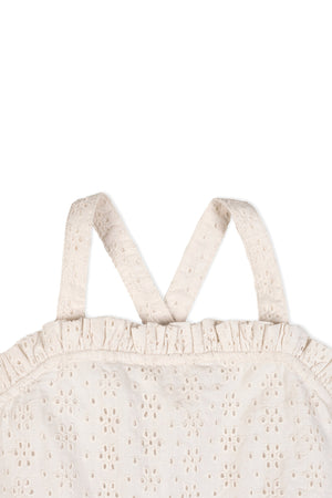 Close-up of the back of a natural-colored dress featuring ruffle edges and cross-back straps, made from organic cotton with eyelet detailing. Ideal for summer wear and environmentally friendly.