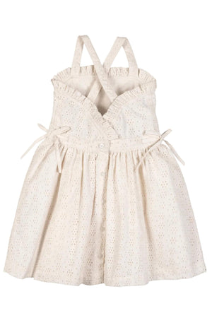 A light beige organic cotton dress features ruffle edges, cross-back straps, and a button closure down the center. This airy eyelet dress is perfect for summer adventures.