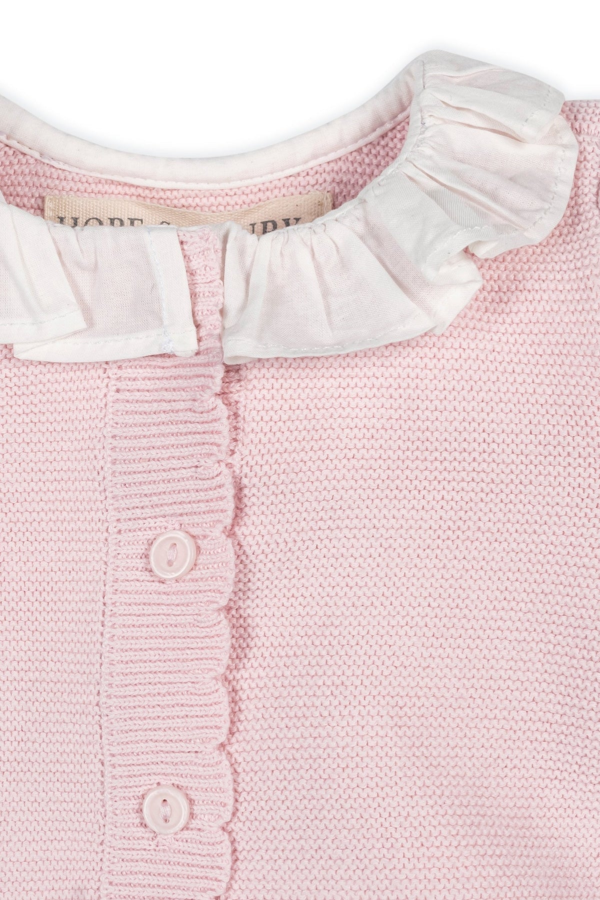 Close-up of a pale pink organic cotton romper featuring a delicate ruffle collar, scalloped trim, and button front closure, perfect for babies and crafted for comfort.