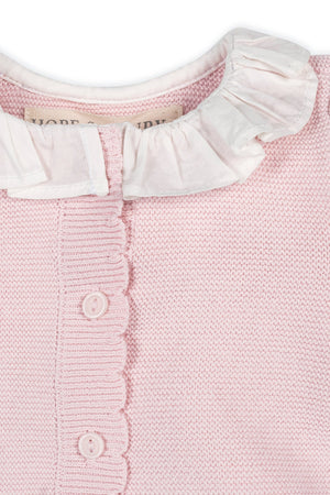 Close-up of a pale pink organic cotton romper featuring a delicate ruffle collar, scalloped trim, and button front closure, perfect for babies and crafted for comfort.