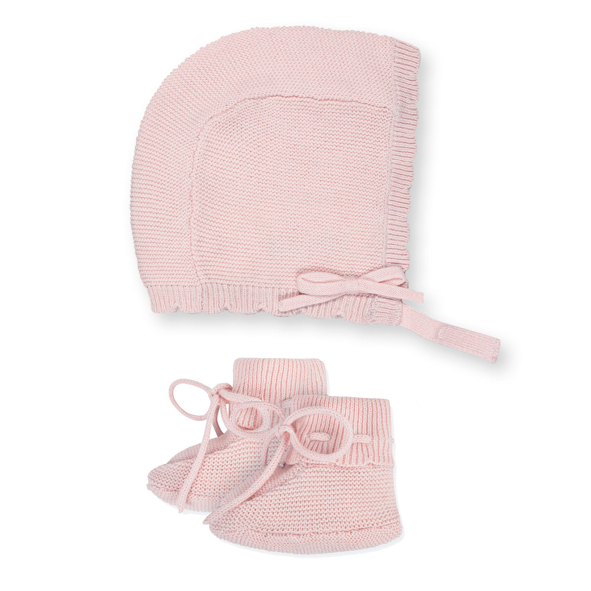 A pale pink knitted bonnet with a tie closure is displayed alongside matching booties featuring a round shape and bow detail, both made from soft, organic cotton for baby comfort.