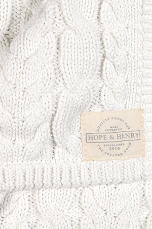 Close-up of a soft white organic cotton cable knit blanket featuring a textured pattern. The label reads Hope & Henry, highlighting its quality and sustainable attributes.
