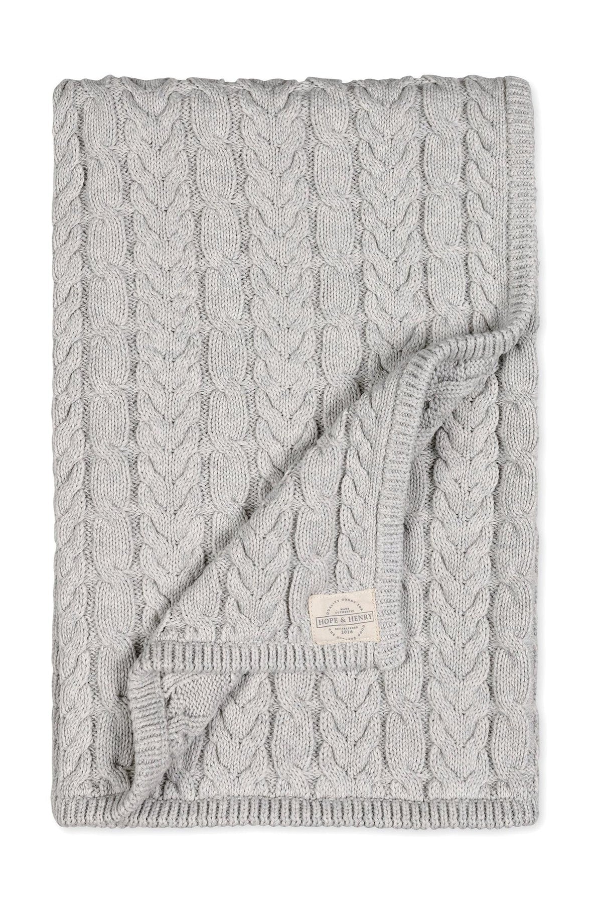 A light gray organic cotton cable knit baby blanket features a chunky design, perfect for cozy cuddles and outdoor outings. The blanket is soft, sustainable, and ideal for infants.