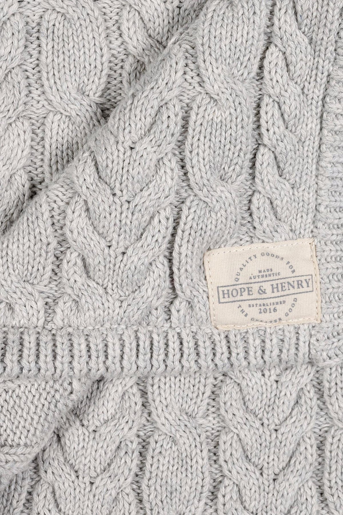 Light gray organic cotton cable knit blanket featuring a textured design. The blanket is branded with a Hope & Henry label, showcasing its soft, eco-friendly material and timeless style.