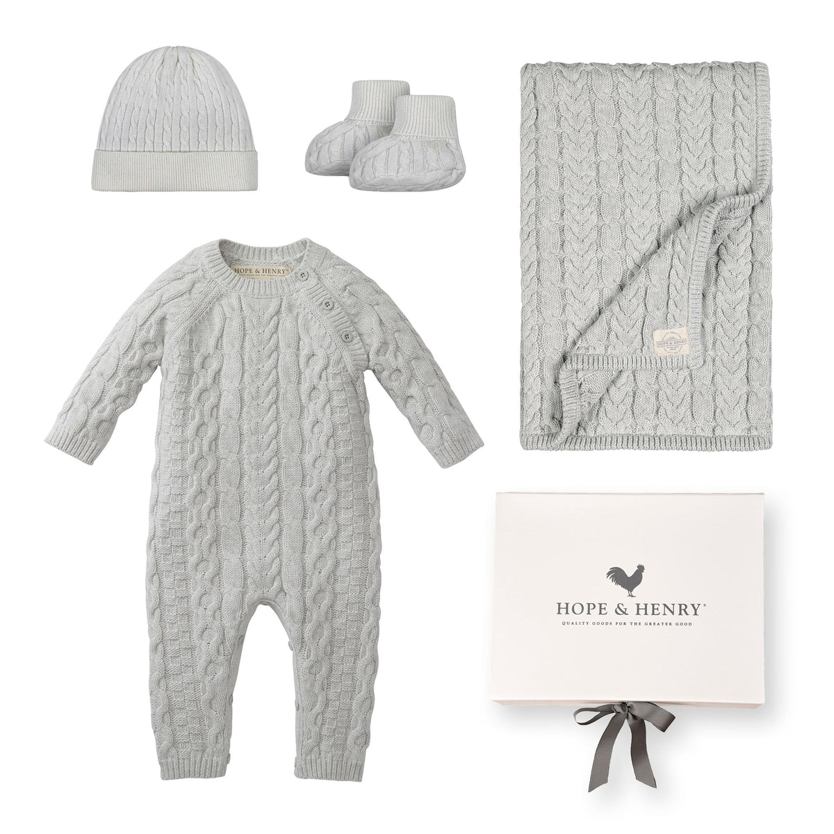A light gray organic cotton cable romper, matching beanie, booties, and a blanket are neatly arranged beside a branded gift box. This sustainable baby gift set is perfect for newborns.