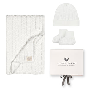 A cozy snow white cable knit blanket, matching beanie, and booties are displayed alongside a beautifully packaged gift box labeled Hope & Henry.
