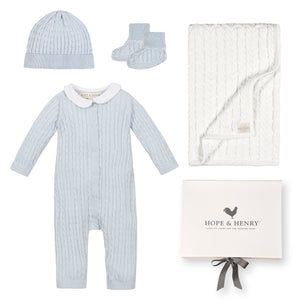A pale blue baby romper with a Peter Pan collar, accompanied by a matching beanie, booties, and a white cable-knit blanket, all presented in a gift box by Hope &.
