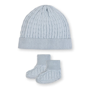 A pale blue knitted beanie and matching booties are displayed together. Both pieces feature a textured cable knit design, perfect for keeping babies warm and cozy in soft, organic cotton.