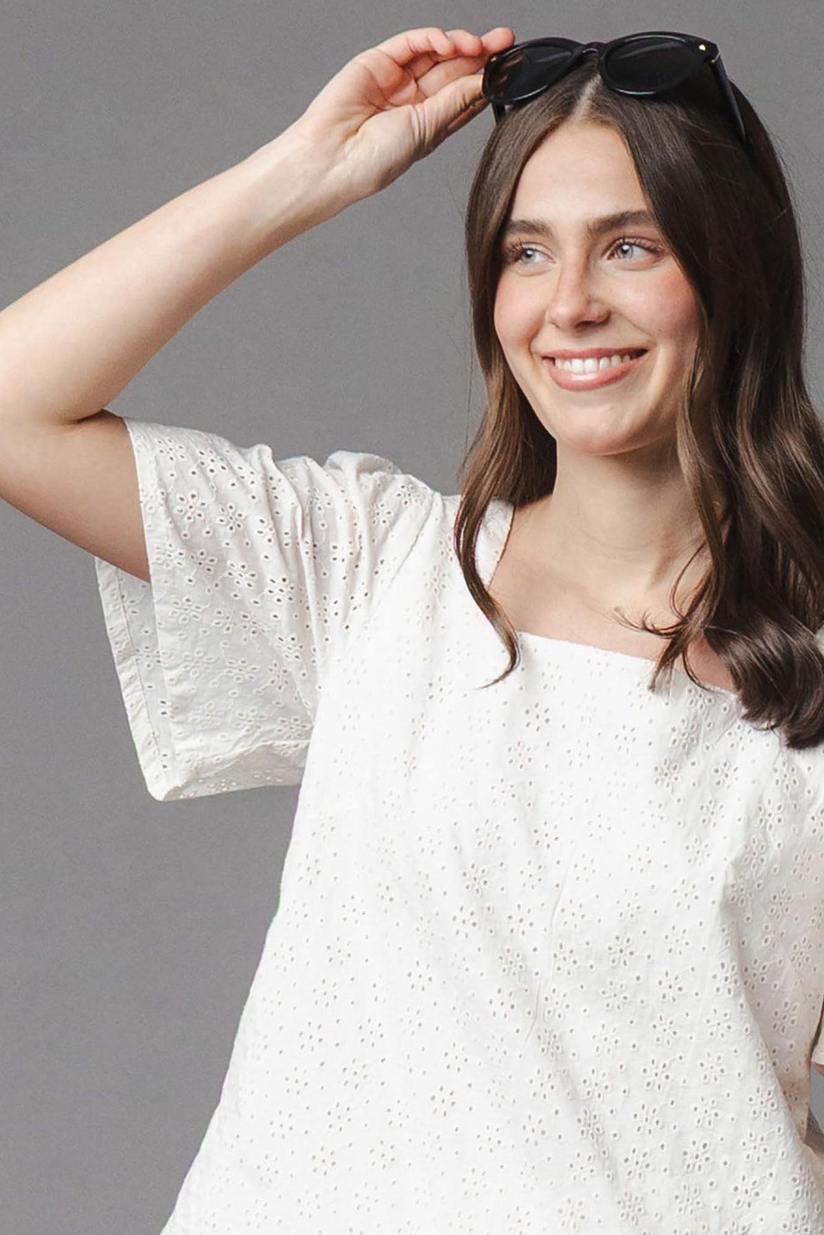 A woman smiles while wearing a white organic cotton flounce sleeve top featuring eyelet detailing. The relaxed fit and airy fabric make it ideal for warm weather occasions.