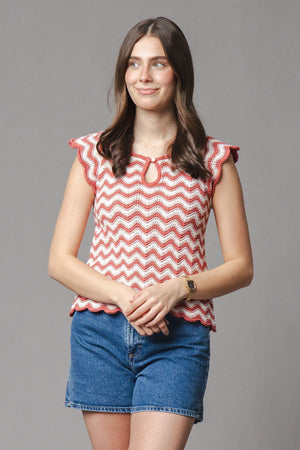 A woman wearing a red and white organic cotton flutter sleeve sweater top with a keyhole closure poses against a neutral background, paired with denim shorts for a casual summer.