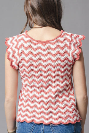 A woman is shown from the back wearing a coral and white organic cotton sweater top with flutter sleeves and a textured wave pattern, set against a neutral gray background.