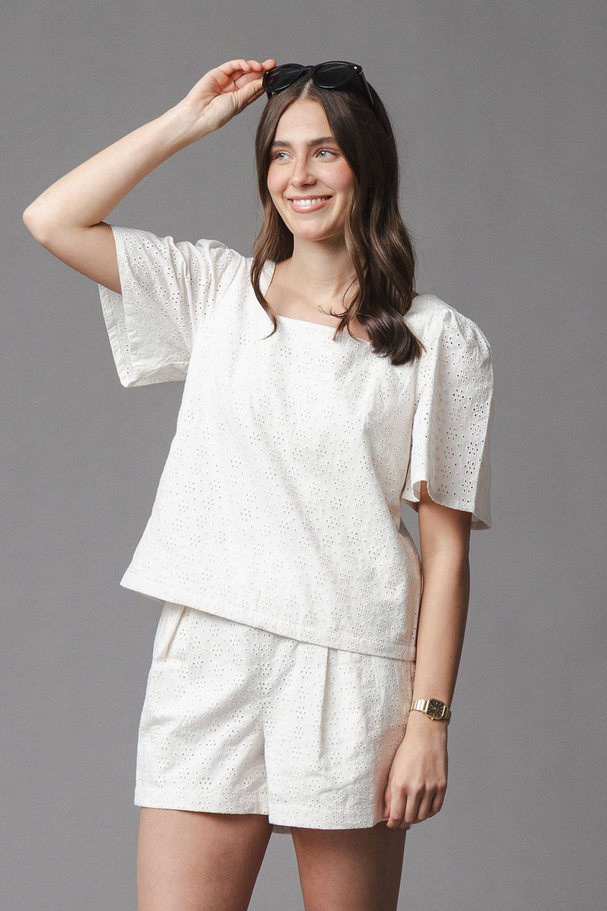 A woman is wearing a light, organic cotton eyelet matching outfit featuring a square-neck top and cinched waist shorts.