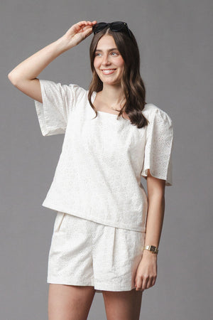 A woman is wearing a light, organic cotton eyelet matching outfit featuring a square-neck top and cinched waist shorts.