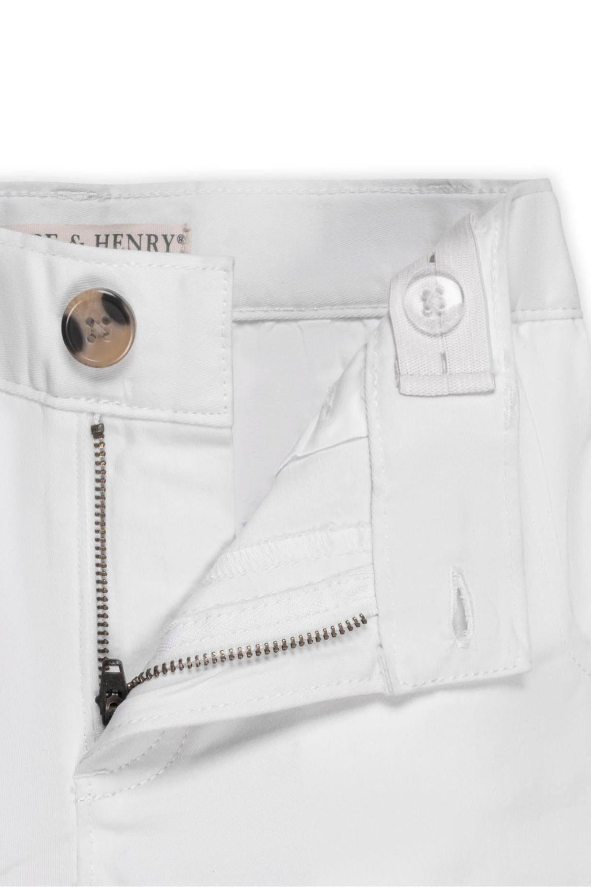 Close-up of white organic cotton chino pants featuring a faux horn button, zipper, and adjustable waistband for baby boys.