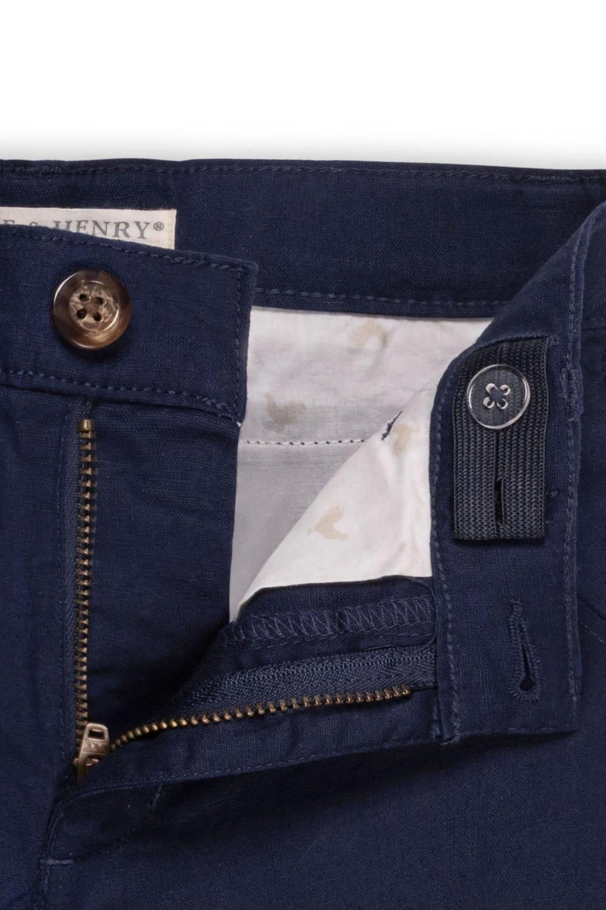 Close-up of navy linen shorts featuring a zipper, a faux tortoise button, and adjustable waistband details.