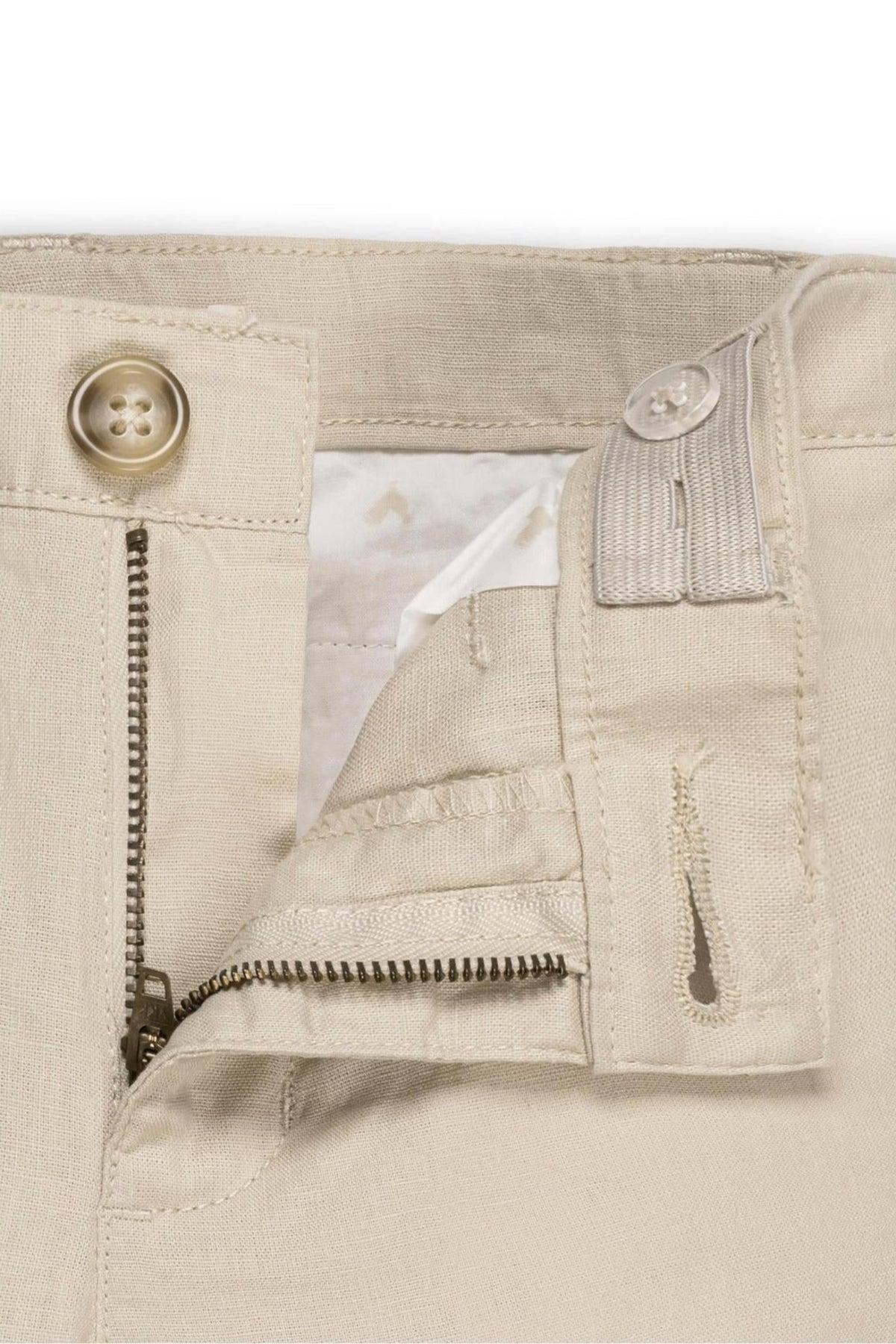 Close-up of beige linen pants showing a zip fly, faux tortoiseshell button, and adjustable waistband for a comfortable fit.