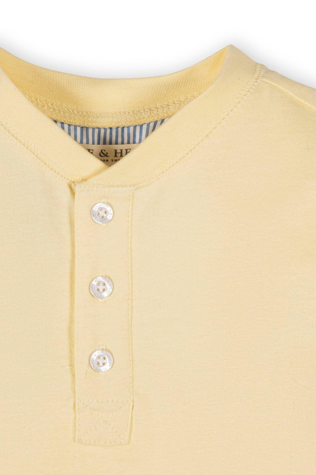 Close-up of a pale yellow organic cotton henley t-shirt featuring a button placket and a soft, smooth texture.