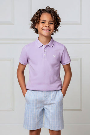 A smiling boy wears a lavender organic cotton polo shirt and light blue plaid shorts, standing against a white backdrop.