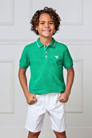 A smiling boy wears a Kelly green organic cotton polo shirt with a flat-knit collar, paired with white shorts.