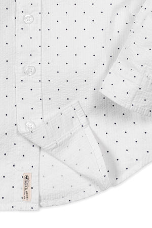 Close-up of a white organic cotton shirt featuring navy blue polka dots, with buttons and a tag from Hope &.