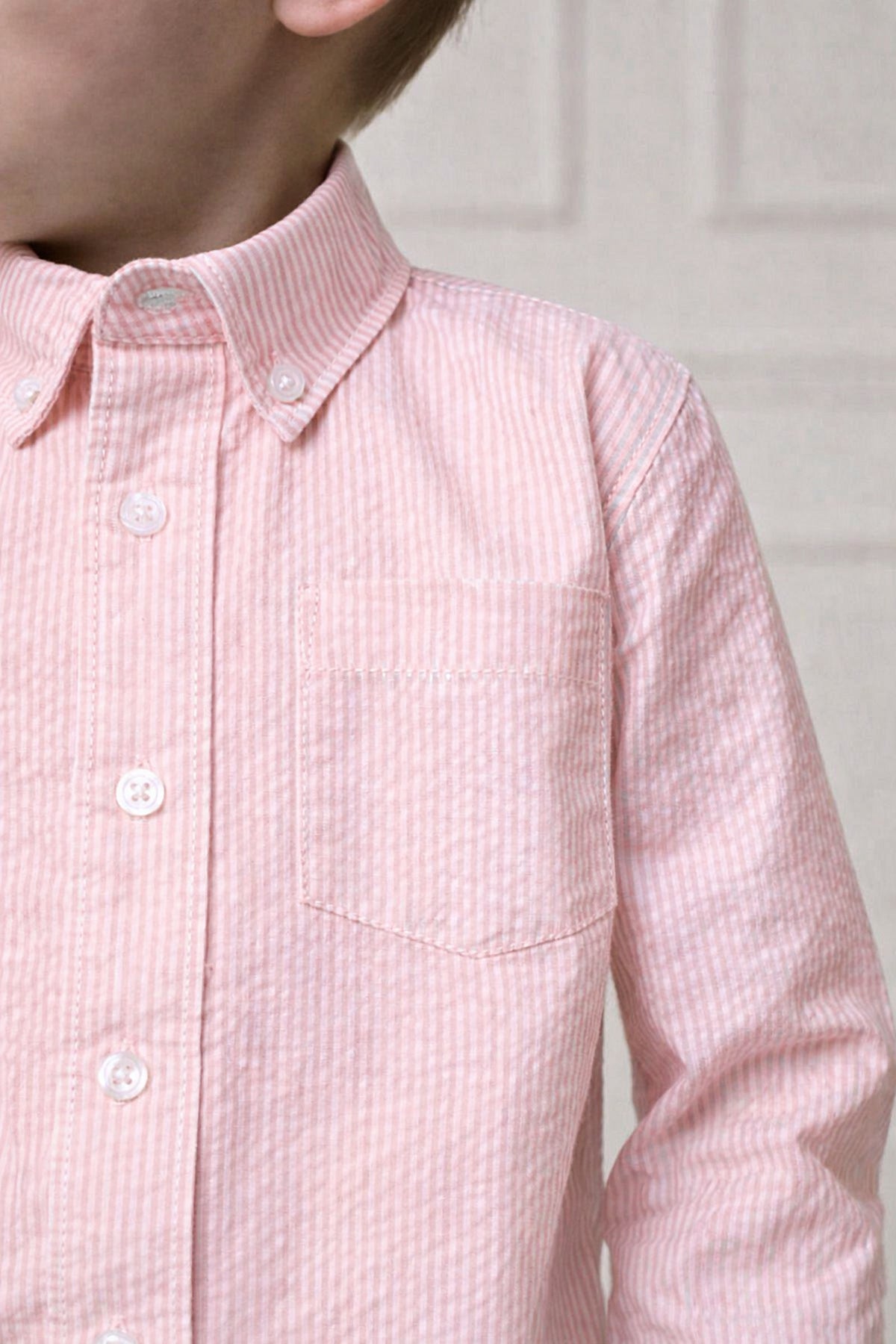 Close-up of a boys long-sleeve, pink seersucker shirt featuring a button-down collar and a chest pocket.