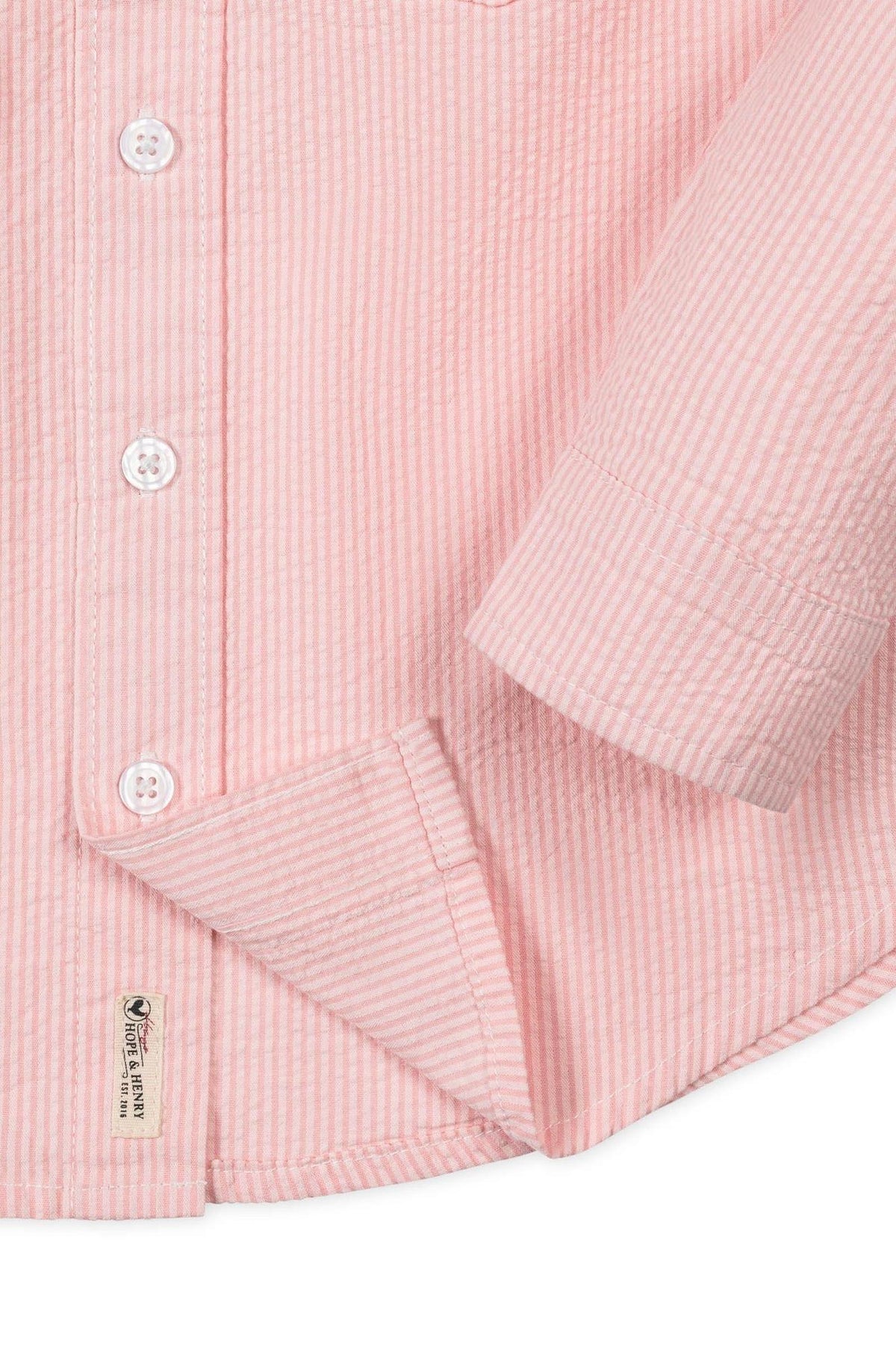 Close-up of a light pink seersucker shirt with white stripes, featuring button closures and a brand label from Hope &.