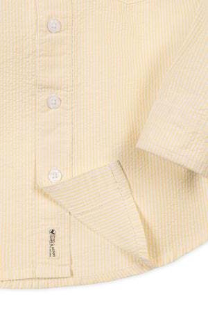 Close-up of a yellow striped button-down shirt made from organic cotton, featuring a chest pocket and soft, textured fabric.