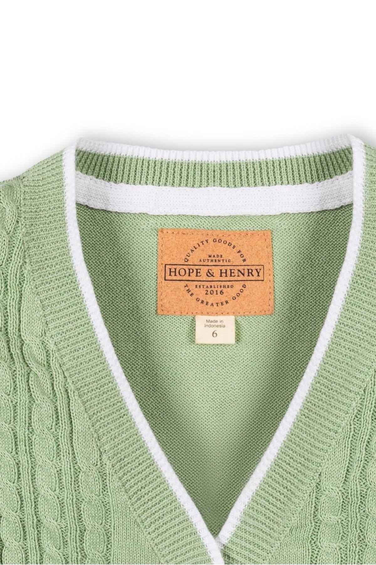 Close-up of a soft green cable knit cardigan with a white ribbed collar and label, designed by Hope & Henry,.