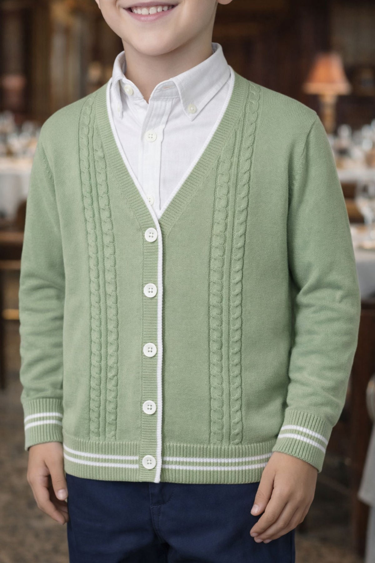 A boy wearing a soft green cable knit cardigan over a white shirt, featuring faux horn buttons and striped rib.