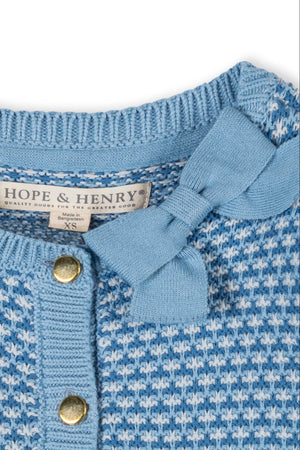 Close-up of a blue tweed stitch cardigan by Hope & Henry, featuring a bow detail at the collar and gold button closure.