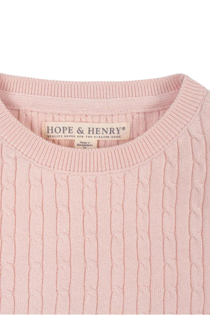 Close-up of a light pink short sleeve cable sweater by Hope & Henry, made from 100% organic cotton. The textured knit pattern is visible, showcasing its soft and sustainable material.