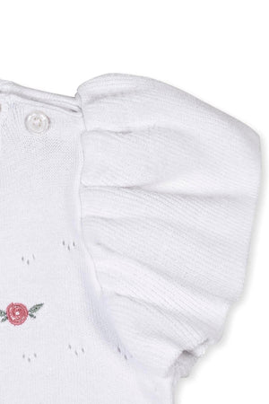 Close-up of a white organic cotton sweater featuring ruffle sleeves and a delicate pink rose embroidery detail.
