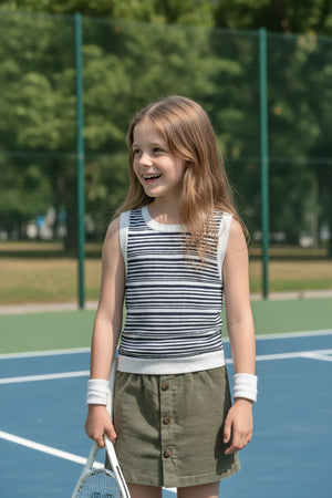 A smiling girl with long hair wears a navy and white striped tank top and a button-up olive skirt, holding.