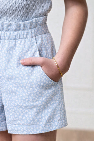A close-up of a childs hand in a pocket of light blue shorts with a delicate white floral pattern.