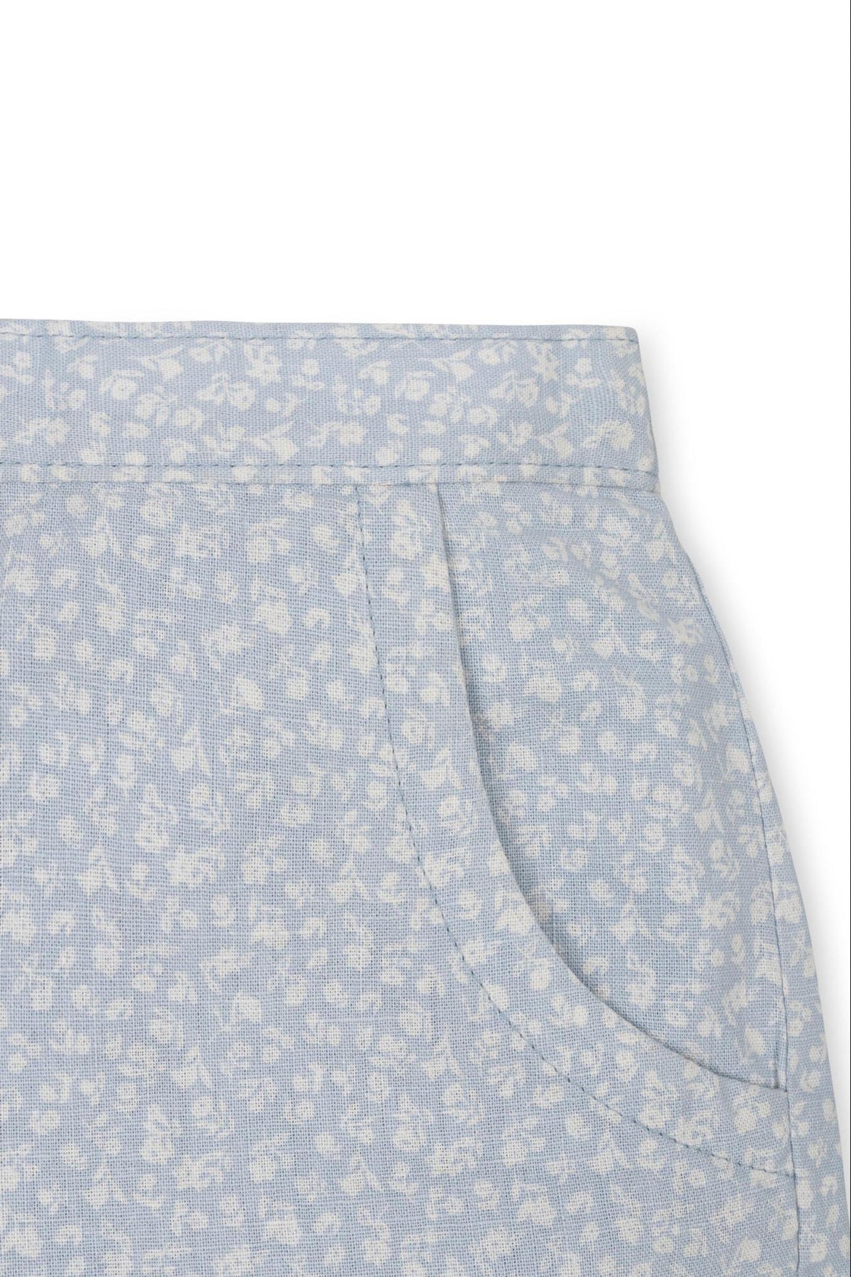 Close-up of light blue linen shorts featuring a white floral pattern and side pockets, designed for comfort and style.