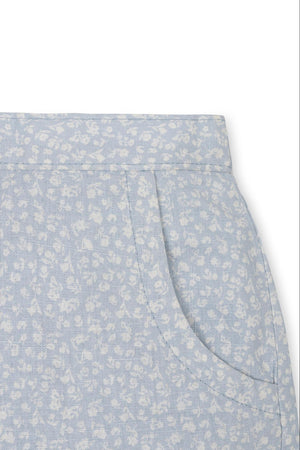 Close-up of light blue linen shorts featuring a white floral pattern and side pockets, designed for comfort and style.