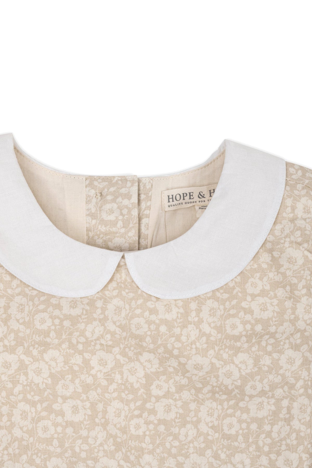 Close-up of a sandy floral dress featuring a white Peter Pan collar and the Hope & Henry label.